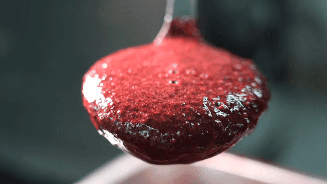 Red raspberry sauce scooped out with ladle