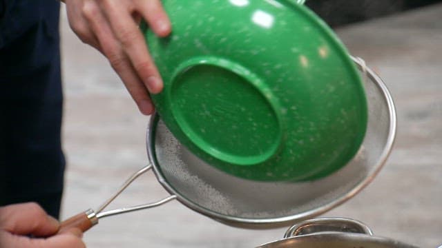 Noodles taken from hot broth are strained through a sieve and placed in a bowl