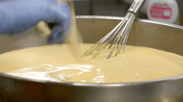 Baker mixing dough in large metal bowl
