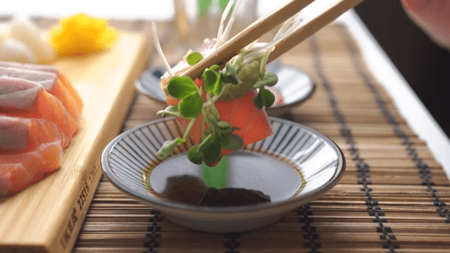 Scene where salmon sashimi is topped with wasabi and radish sprouts and dipped in soy sauce