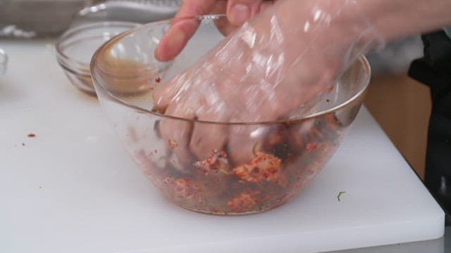 Hands wearing plastic gloves preparing abalone in a glass bowl