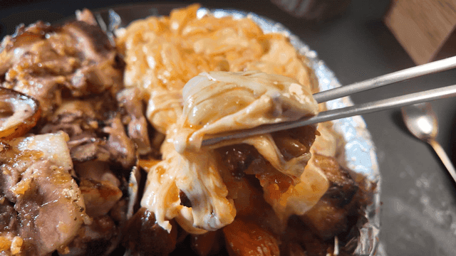Chopsticks lifting grilled spicy pig's trotters covered in cheese