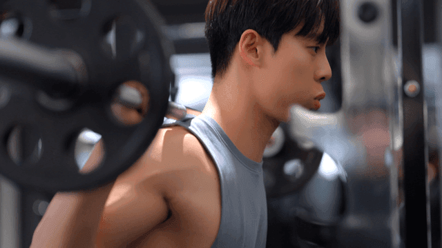 헬스장에서 어깨에 무게를 지고 스쿼트를 하는 젊은 남자