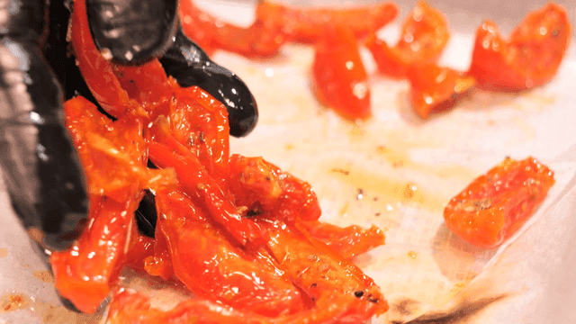Gloved hand handling roasted red tomato