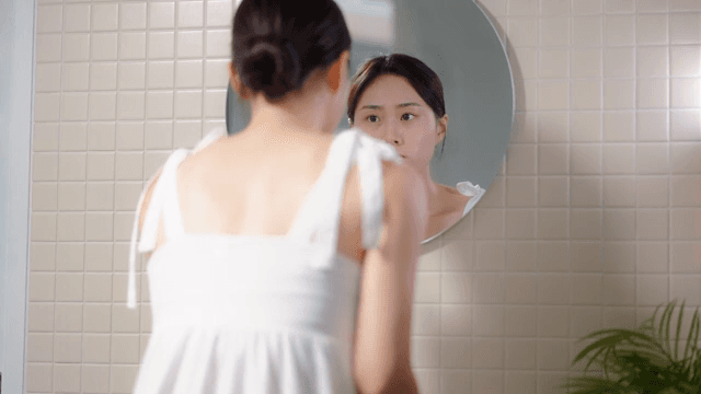 Woman examining her skin in a bathroom mirror