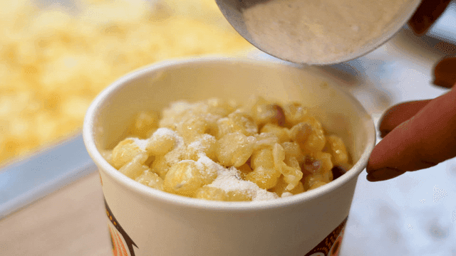 Hand sprinkling cheese powder on buttered corn