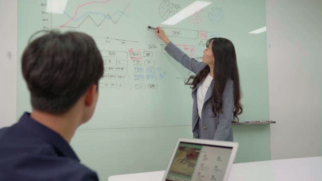 Woman wearing gray blazer presenting on whiteboard in office