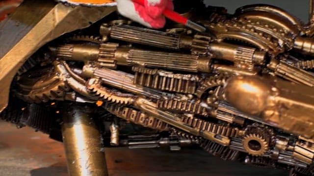 장갑을 낀 손이 미니어처 금속 기계 부품을 칠하는 모습