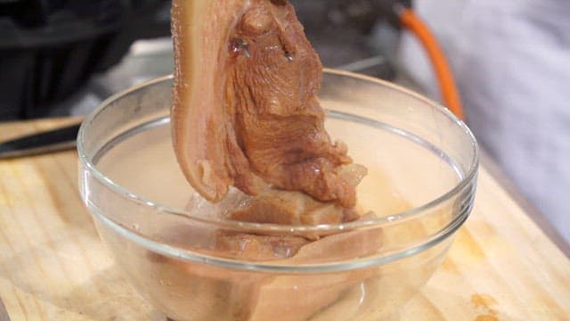 Boiled pork being lifted from a bowl