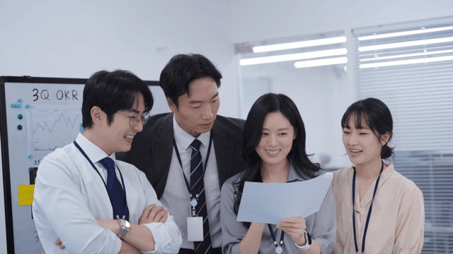 다같이 서서 웃으며 회의 문서를 체크하는 팀원들