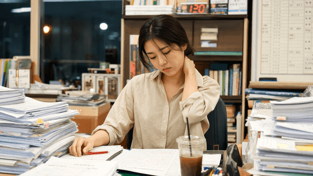 Woman working late at office desk piled high with documents