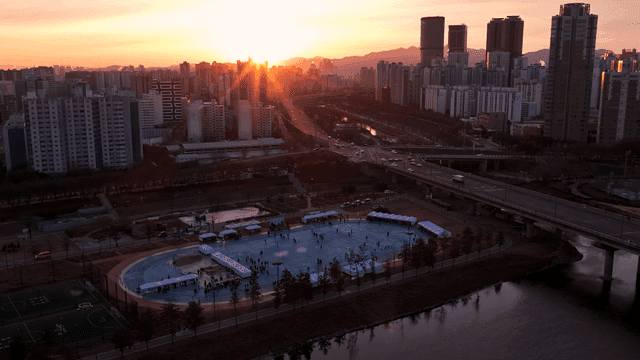 People gathered at sports field in setting sun over bustling city landscape