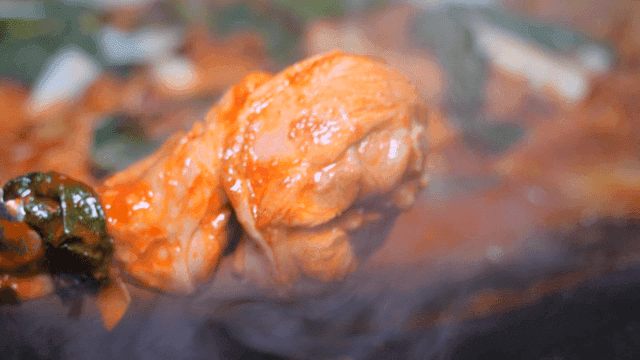 Tongs lifting chicken leg from spicy chicken stew