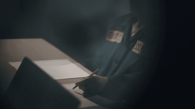 Prisoner sitting at desk writing statement and clock