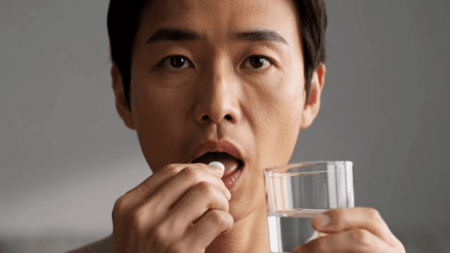 Man taking a pill with a glass of water