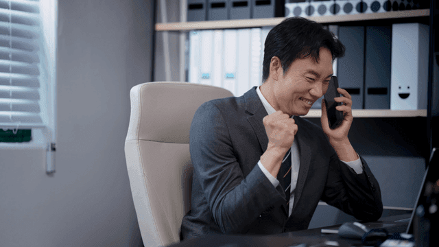 A man cheering while making a phone call in his office