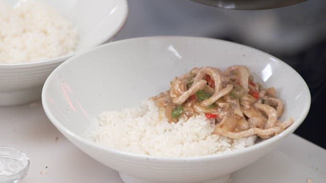 하얀 그릇의 쌀밥 위로 얹어지는 고기 채소 볶음