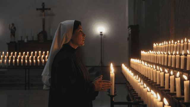 촛불이 켜진 교회에서 기도하는 수녀
