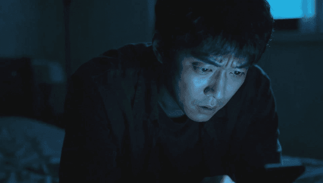 어두운 방에서 휴대폰에 집중하는 남자