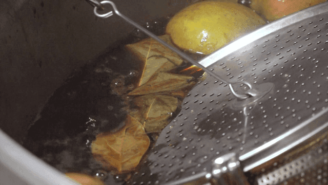 Bay leaves and fruits above boiling soy broth in pot