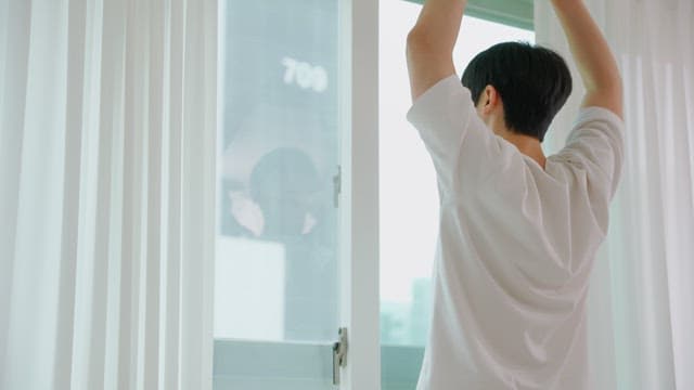 Man Stretching by Window in Morning