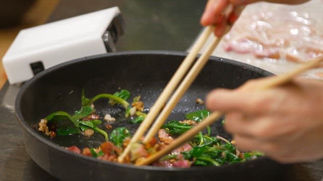 Stir-fryed bacon and spinach being plated on a plate