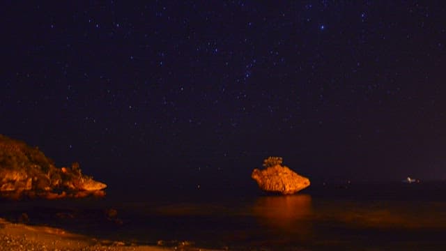 Starry Night Sky Over Seashore and Rock Formation