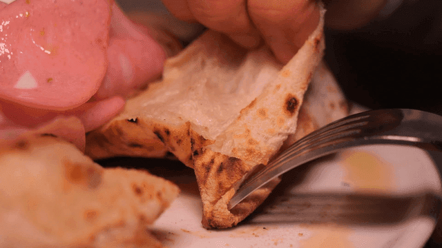 Hands and fork tearing piece of oven-baked pizza on plate