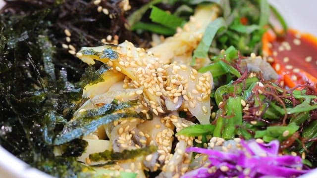 신선한 채소와 전복이 들어간 한국 비빔밥을 숟가락으로 섞는 모습