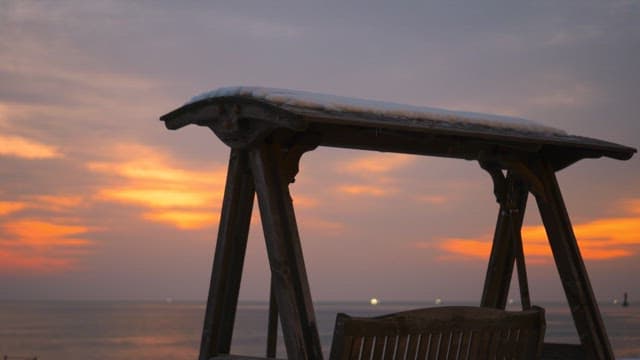 Snow-covered wooden swing under a vibrant sunset