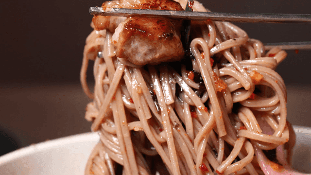 Chopsticks holding noodles with meat