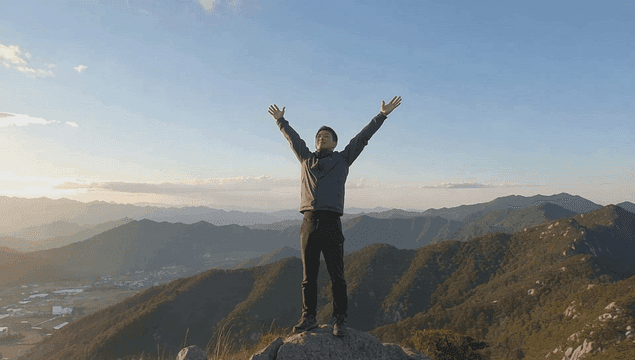 일출에 산 정상에 서 있는 남자