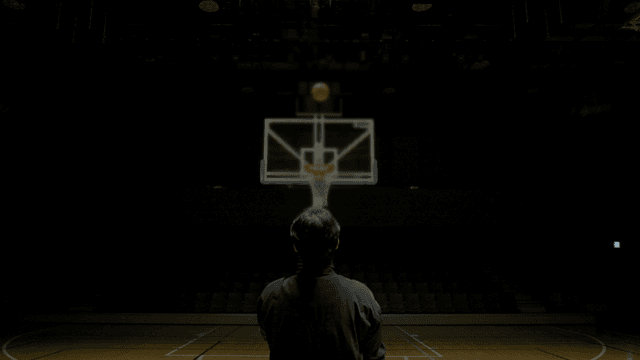 Back view of man throwing ball on indoor basketball court