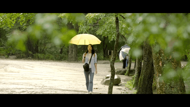 Woman with yellow umbrella in rainy forest