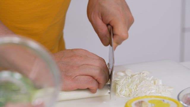 Cutting fresh green onions with a knife on a cutting board