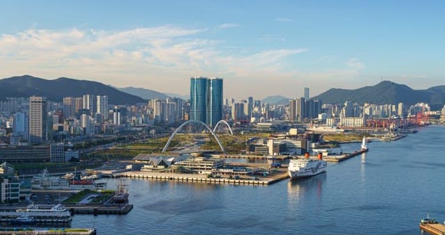 Paranomic view of a bustling port city with tall skyscrapers and bridge from day to evening