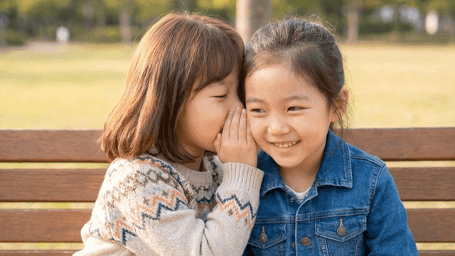 Two girls whispering on a park bench
