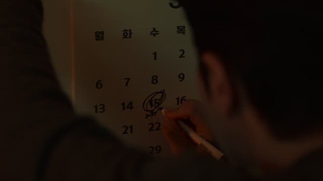 Person marking an important date on a calendar in a dark room