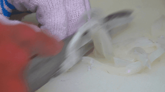 Hands quickly scooping up squid sashimi on cutting board