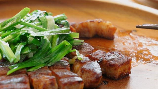 Marinated pork ribs and fresh green onions neatly plated on a wooden plate