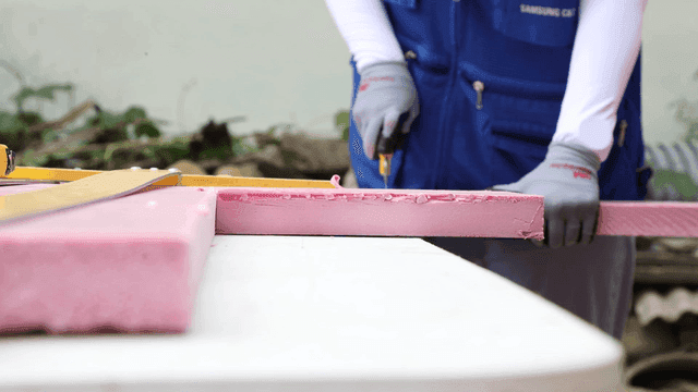 Worker cutting pink foam board outdoors