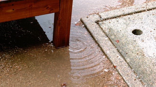 Raindrops falling near a wooden table and concrete block