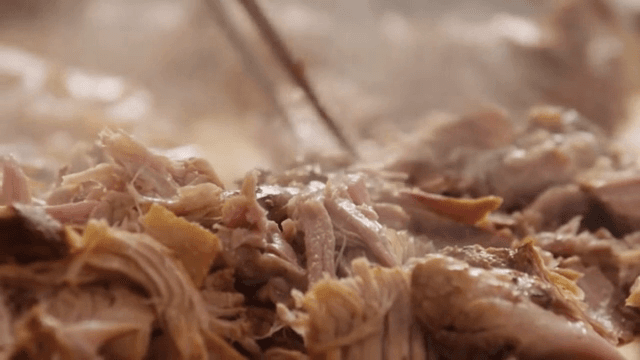Steaming meat being shredded with tongs