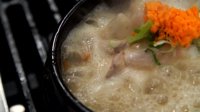 파와 얇게 썬 당근과 함께 끓고 있는 삼계탕