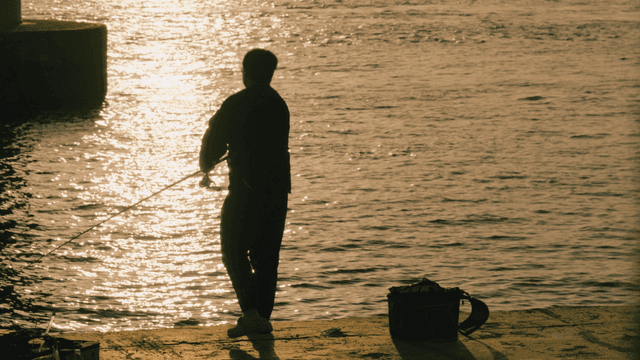 Back of man fishing on riverbank at sunset