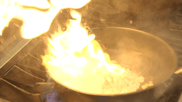 Onions being sautéed in a pan with flames