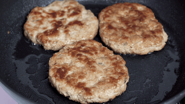 Three meat patties cooking in pan