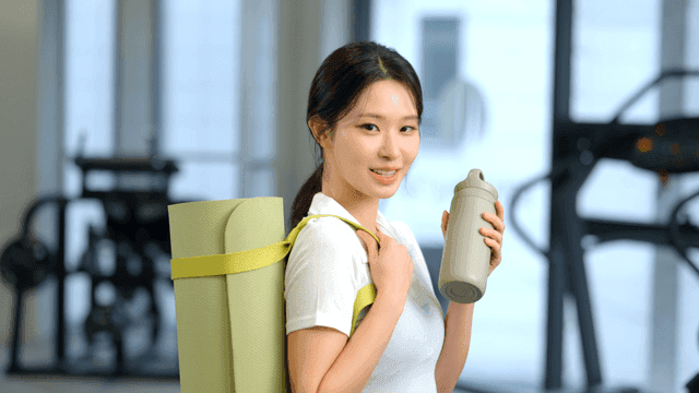 요가 매트와 물병을 들고 헬스장에 있는 여성