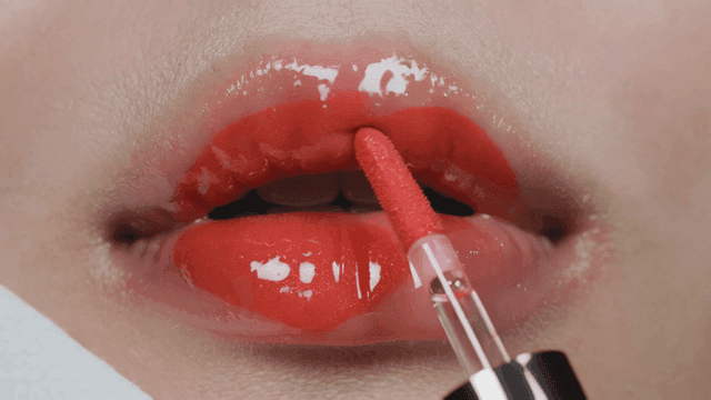 Applying glossy red lip gloss