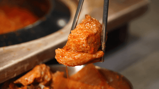 젓가락으로 들어올린 큼직한 김치찌개 돼지고기 조각